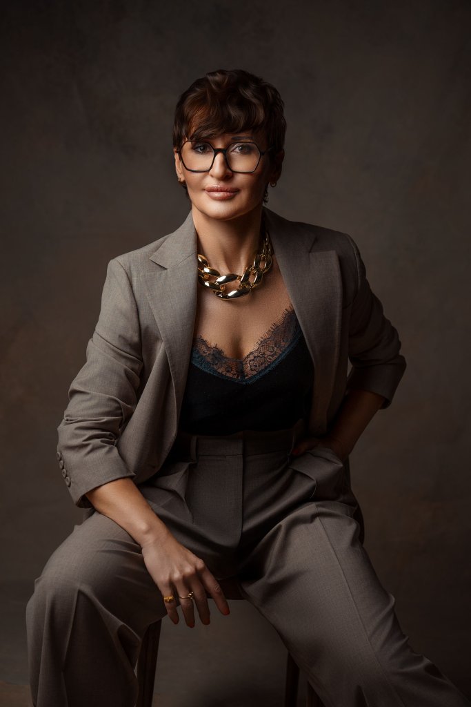 Elegancka sesja kobieca – kobieta w okularach, szarym garniturze, koronkowym topie i złotym naszyjniku