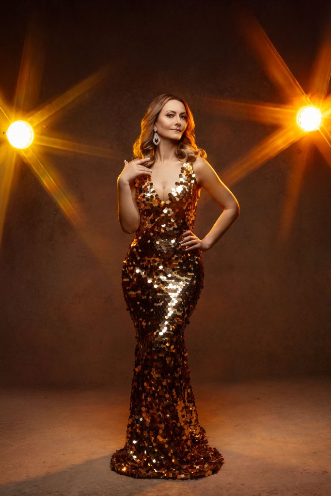 Sesja kobieca glamour – kobieta w złotej cekinowej sukni syrenie w blasku reflektorów